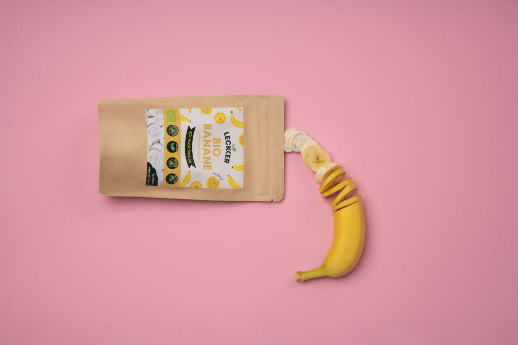 Gefriergetrocknete Banane neben frischer auf pinken Untergrund