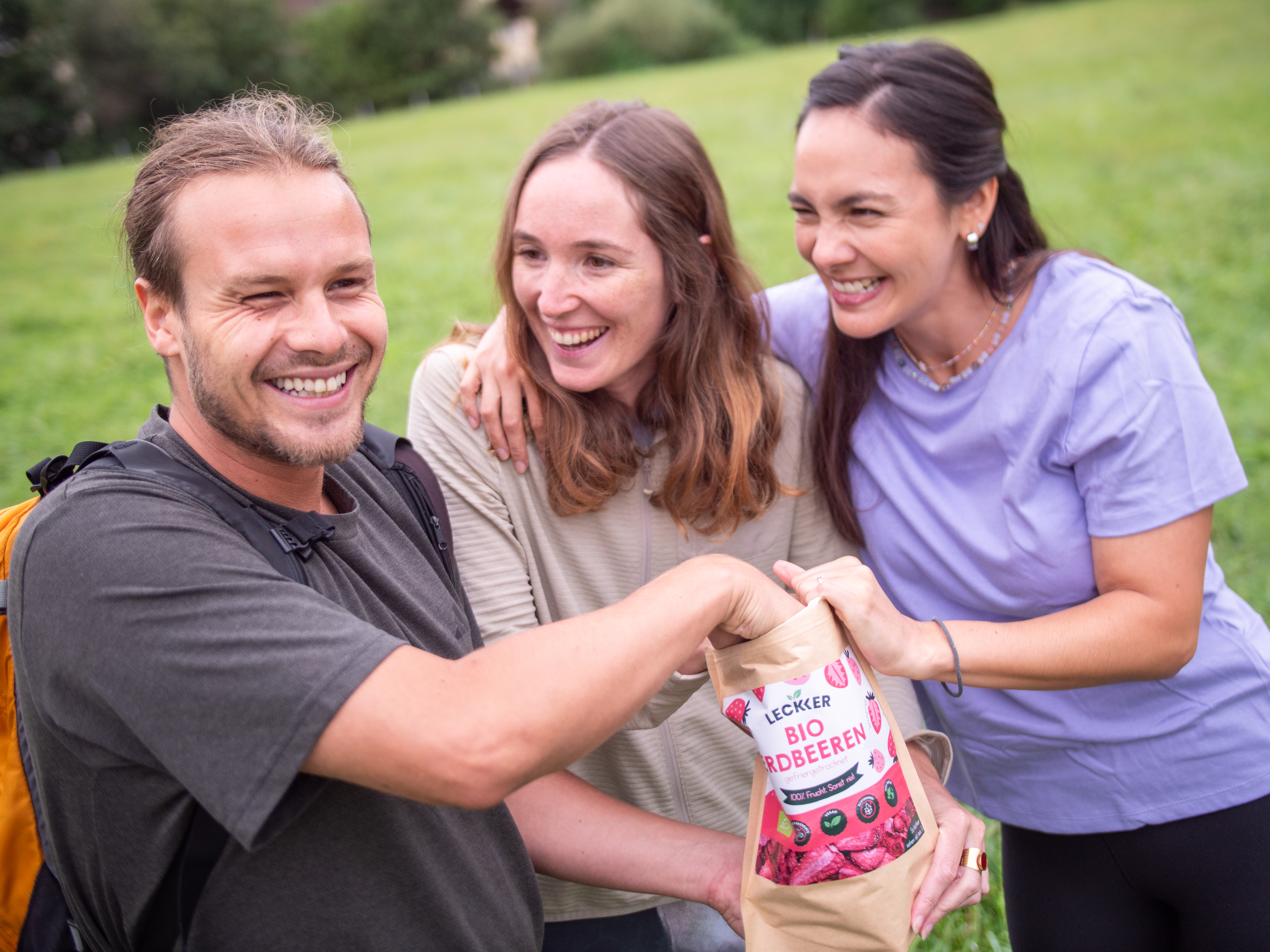 Ein Mann und zwei Frauen beim Wandern mit gefriergetrockneter Erdbeer Packung